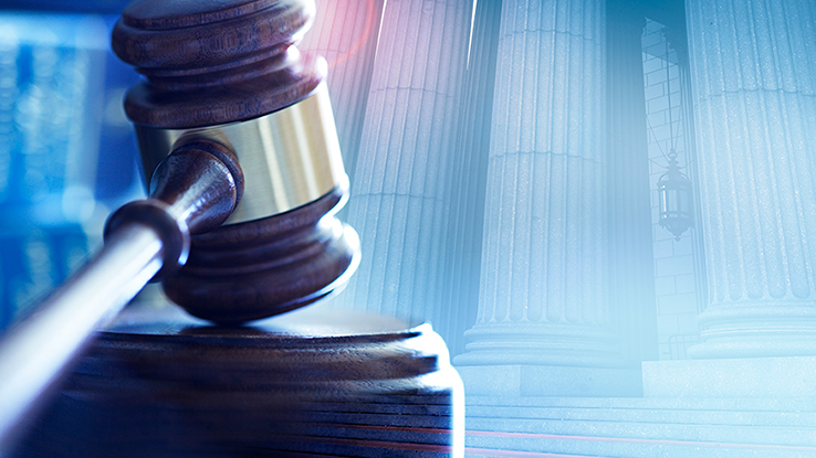 A courtroom gavel with a courthouse in the background.