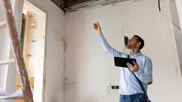 Man Pointing To Ceiling Repairs With Tablet In Hand 