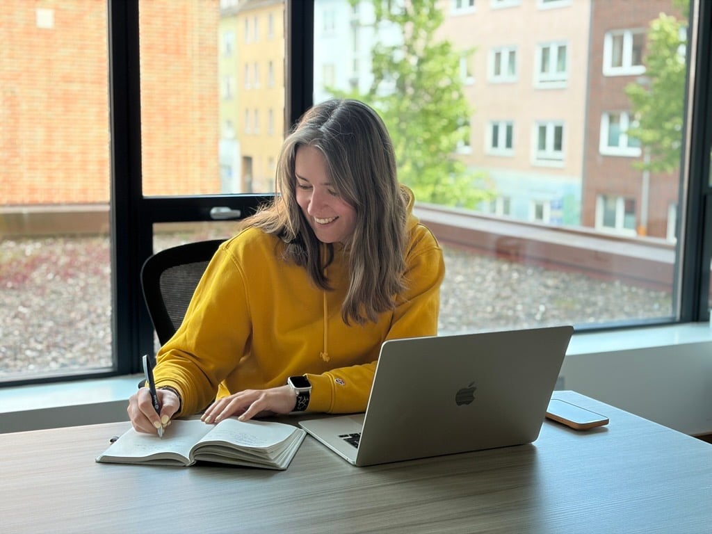 woman-wearing-yellow-writing-in-notebook-laptop