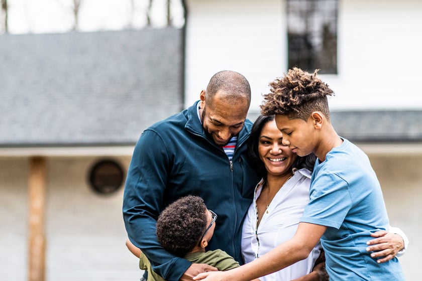 Family Of Four Hugging In Front Of Home 