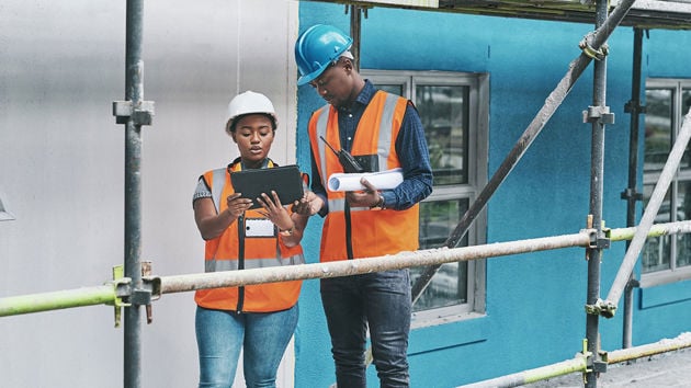 Workers On Scaffolding Reviewing Tablet On Jobsite 
