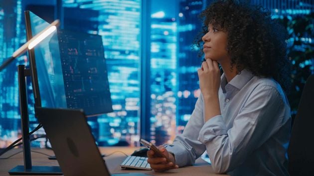 Woman Looking At Computer Holding Phone 