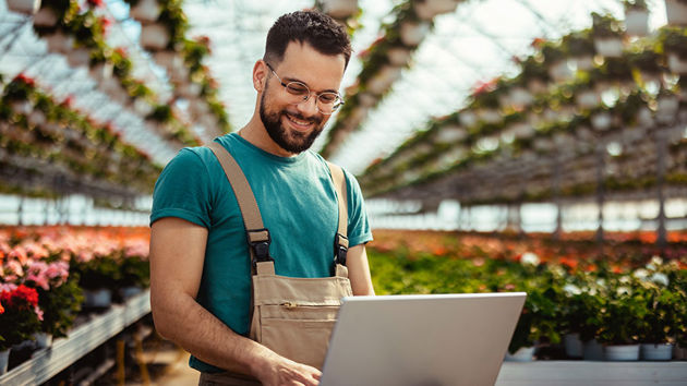 Farmer In Greenhouse Looking At Computer 