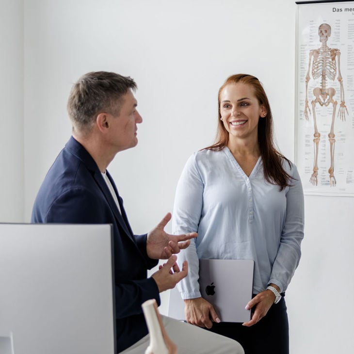 Two People Standing In Front Of An Anatomy Chart 