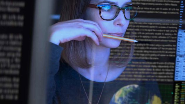 Woman Reading From A Screen With Pencil In Hand 