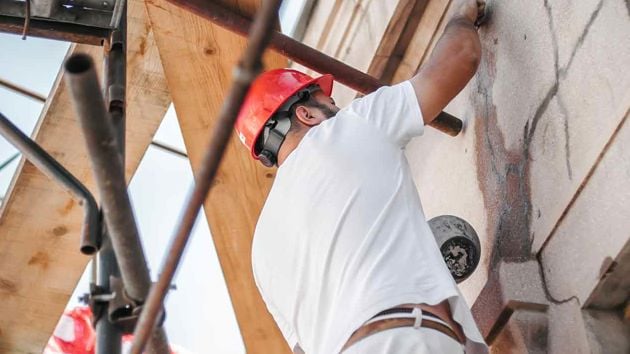 Worker On Scaffolding Repairing Building Facade 