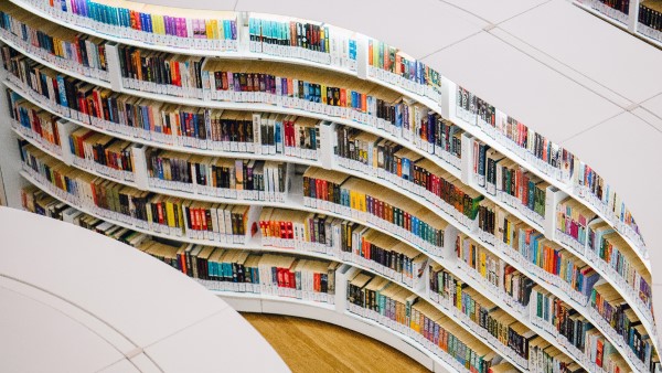 Curving white library shelves photographed from above, with many colorful books on them