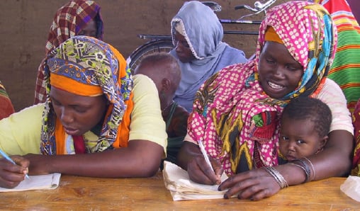 Photo of women in sub-Saharan African community writing at tables 